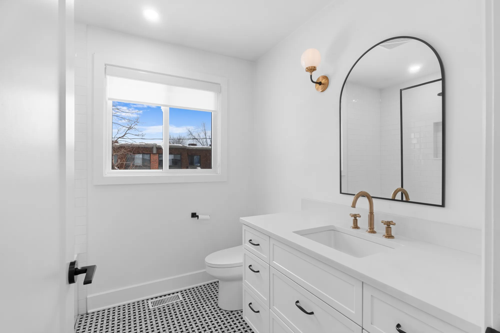 Bathroom vanity with arched mirror and brass sconce